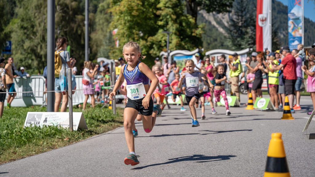 Hochmotiviert und konzentriert laufen die Kinder beim Achensee Kinderlauf in Pertisau, während im Hintergrund die Zuschauer ihnen begeistert zujubeln.