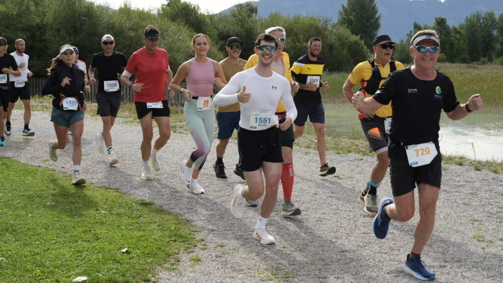 Die Teilnehmer laufen auf der Achenseelauf-Eventstrecke entlang und lachen in die Kamera.